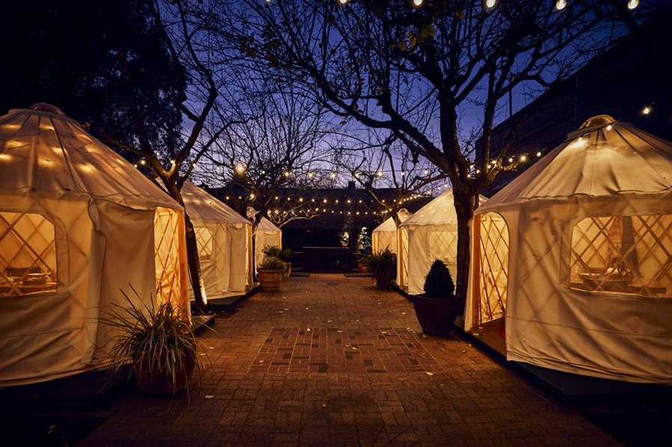 Illuminated tents in a courtyard with string lights and evening sky.