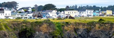 Coastal houses on a cliff above rocky beach with ocean waves.