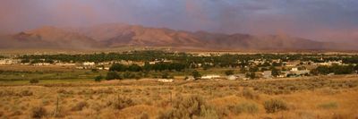 Sunset over a small town with mountains, a light rainbow, and vibrant skies.