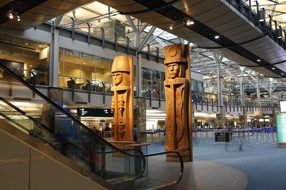 Indigenous totem poles in a modern airport terminal with escalators and high ceilings.