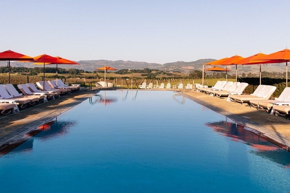 Infinity pool with orange umbrellas, lounge chairs, and a scenic vineyard backdrop.