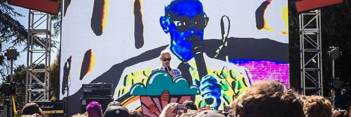 jon waters on stage in front of his own portrait