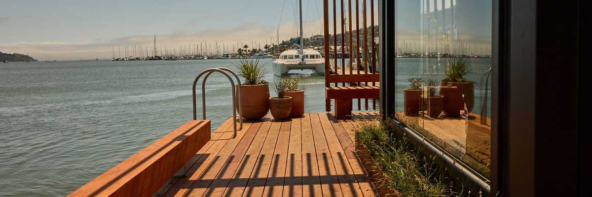 Lakeside deck with potted plants, lattice roof, and moored boats under a clear sky.