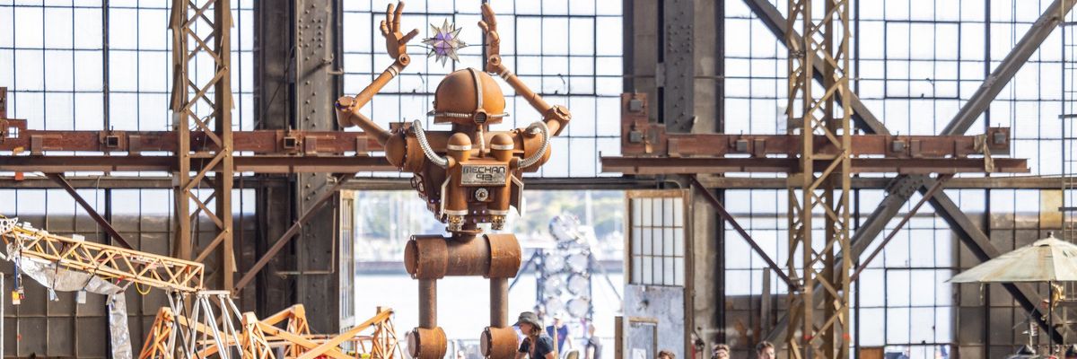 Large crowd at an exhibition with a giant robot sculpture in the background.