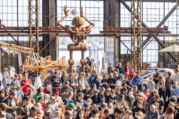 Large crowd at an exhibition with a giant robot sculpture in the background.