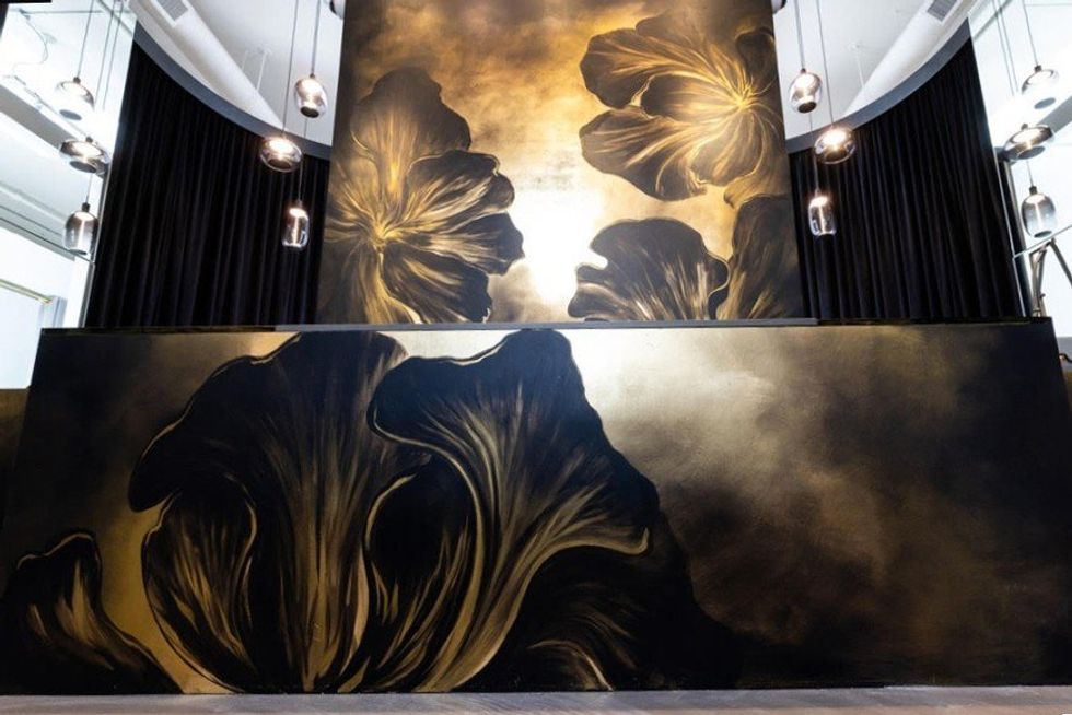Large floral mural with dark gold and black tones in a modern space with pendant lights.