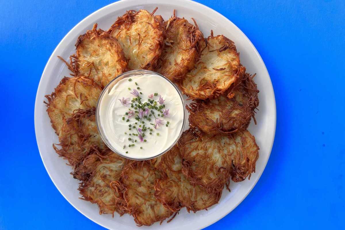 latkes on a plate around a bowl of creme fraiche with flowers on top