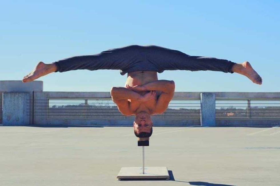 Man performing a handstand split on a rooftop, arms crossed over chest.
