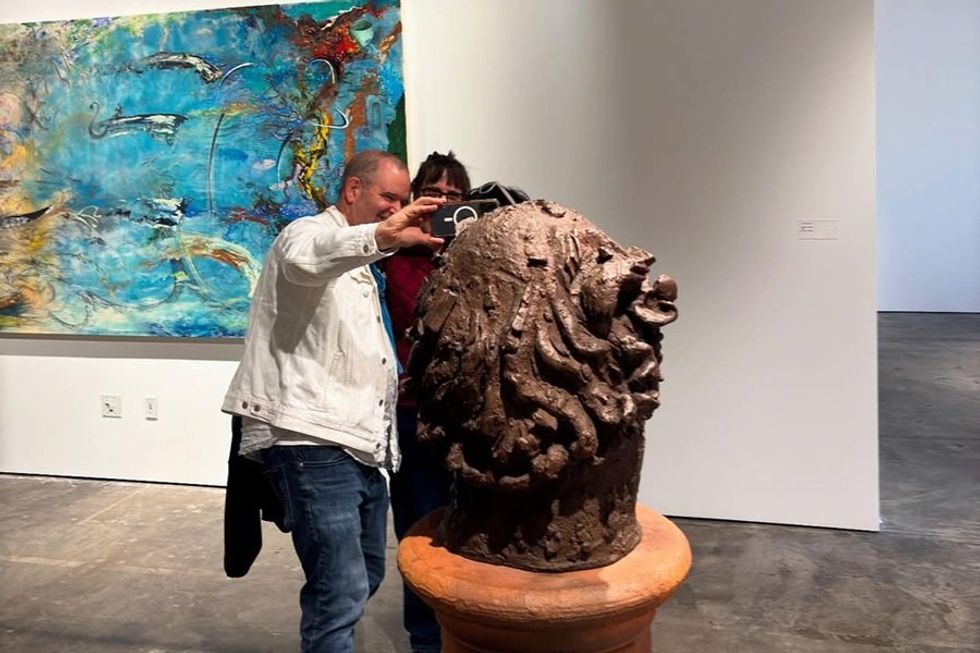Man photographing a sculpture in an art gallery next to a vibrant abstract painting.