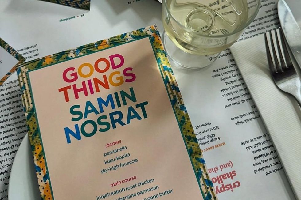 Menu with "Good Things" title beside a drink and cutlery on a table.