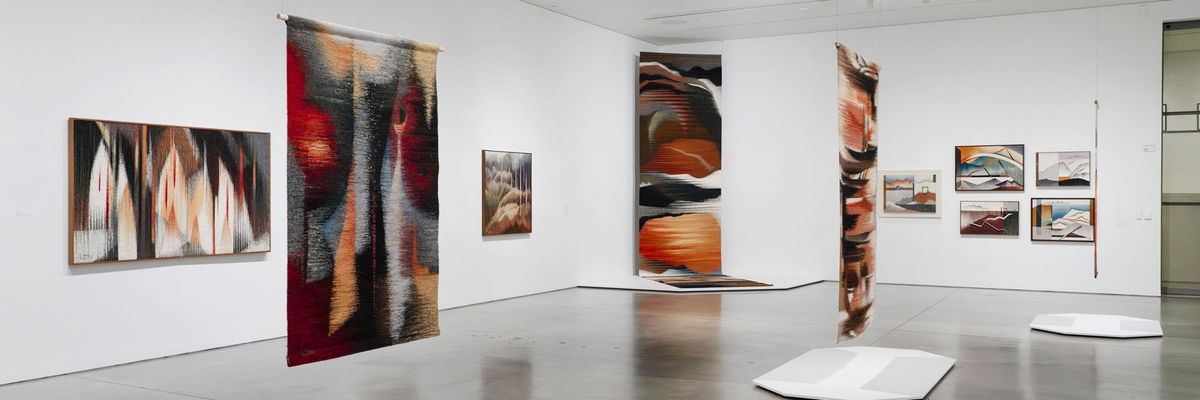 Modern art gallery with abstract woven tapestries and paintings displayed on white walls.