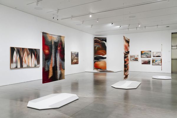 Modern art gallery with abstract woven tapestries and paintings displayed on white walls.