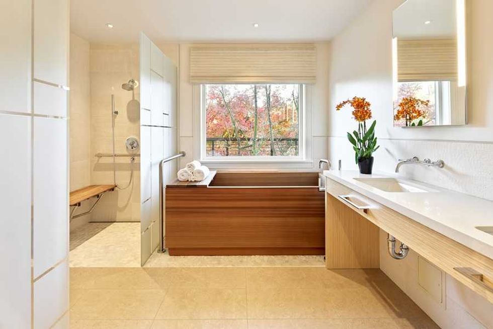 Modern bathroom with a wooden tub, large sink, and window view of autumn trees.