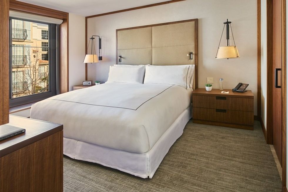 Modern hotel room with a neatly made bed, bedside tables, and large window.