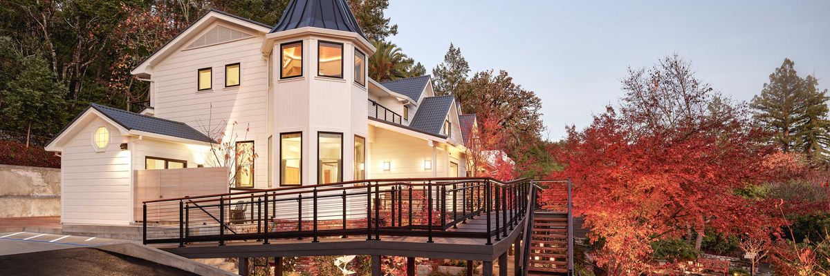 Modern house with a turret, surrounded by autumn trees and enhanced by evening lighting.