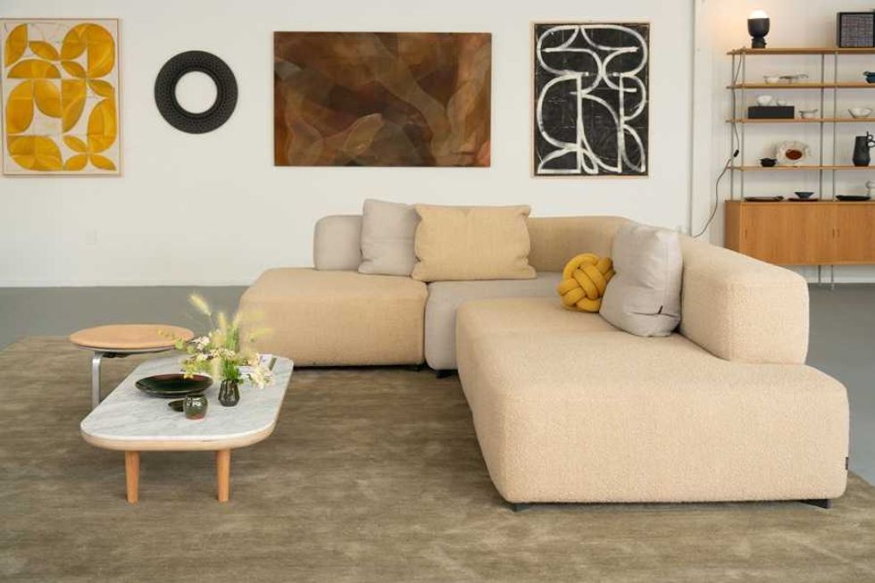 Modern living room with beige sectional sofa, artworks, and a marble coffee table.