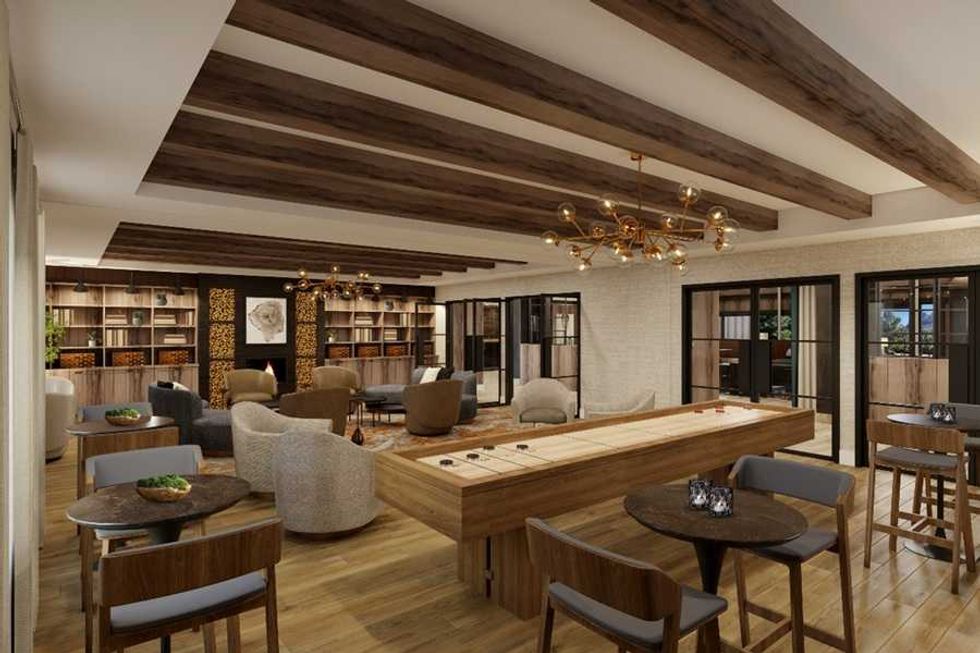 Modern lounge with wooden beams, cozy chairs, tables, and a library wall.