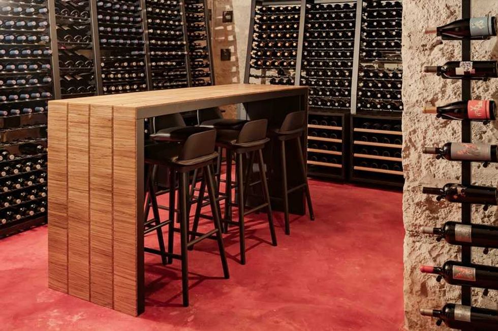 Modern wine cellar with wooden bar, chairs, and racks of wine bottles.