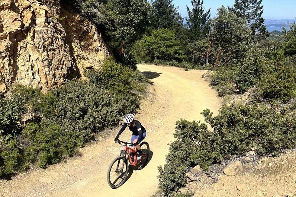 Mountain biker on a winding dirt trail with surrounding trees and rocky terrain.