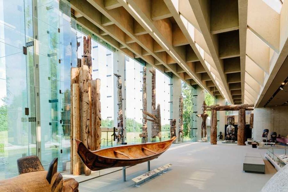 Museum interior with wooden artifacts and a canoe displayed by large glass windows.