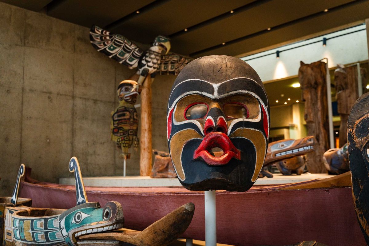 Native mask and totem pole exhibit at a museum with traditional carvings and canoe.