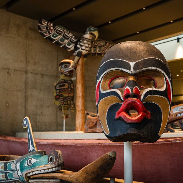 Native mask and totem pole exhibit at a museum with traditional carvings and canoe.