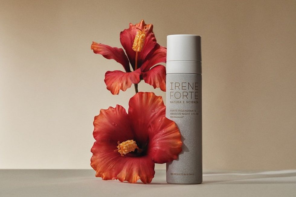 Night cream bottle with vibrant red hibiscus flowers on a neutral background.