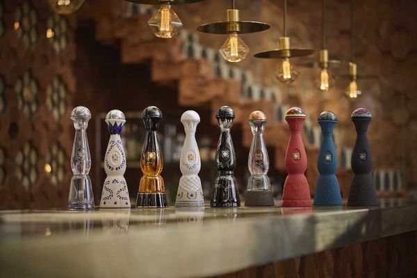 Nine ornate tequila bottles on a bar under pendant lights.