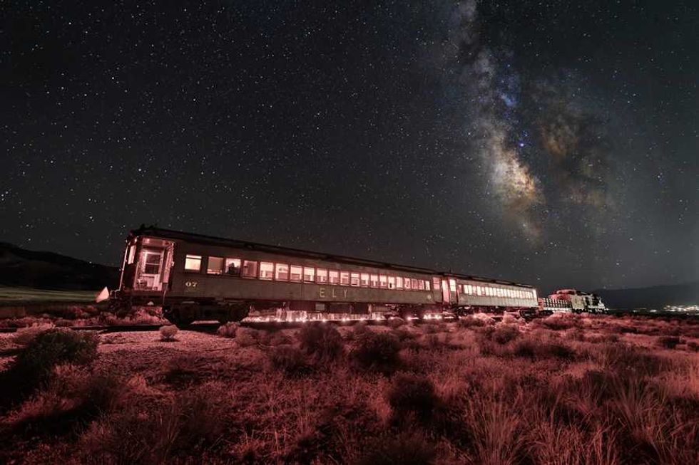 Old train under a starry sky with the Milky Way, illuminated by red ground lighting.