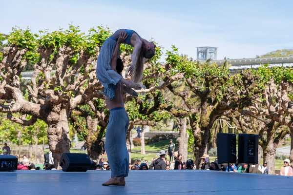 One dancer lifting another on stage in a park