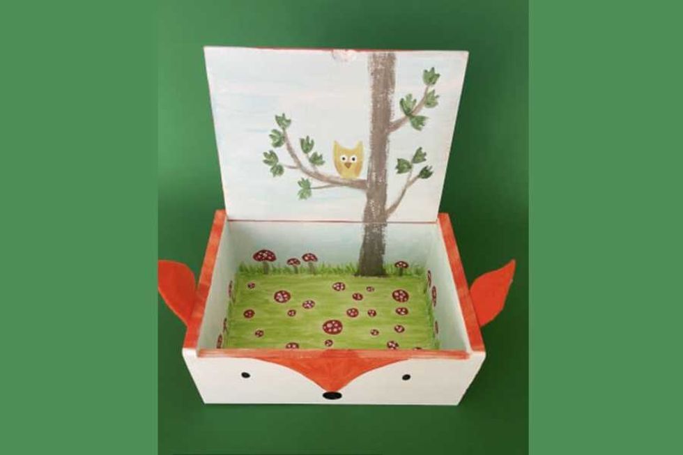 Open box with fox face, painted owl tree lid, mushroom grass interior, on green background.