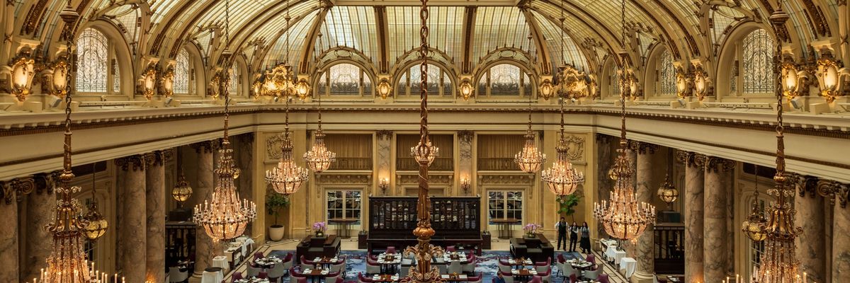 Opulent dining room with chandeliers under a grand, arched glass ceiling.