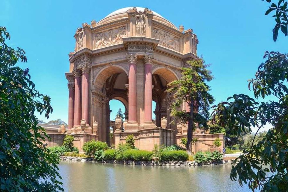 Ornate rotunda with tall columns and a dome, surrounded by greenery and water.