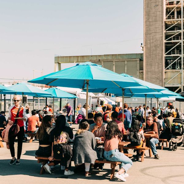Outdoor market with people sitting at tables under bright blue umbrellas.