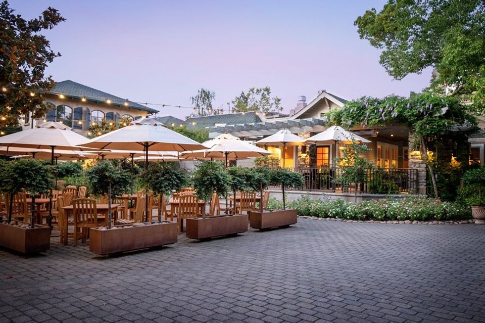 Outdoor patio dining with umbrellas, wooden tables, and lush greenery at sunset.