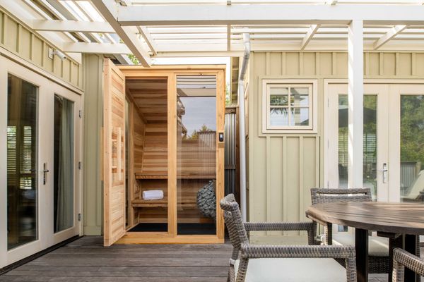 Outdoor patio with a wooden sauna cabin and wicker chairs around a circular table.