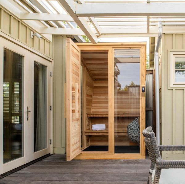 Outdoor patio with a wooden sauna cabin and wicker chairs around a circular table.