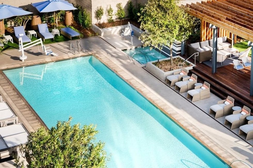 Outdoor pool with deck chairs, blue umbrellas, and wooden patio lounge area.