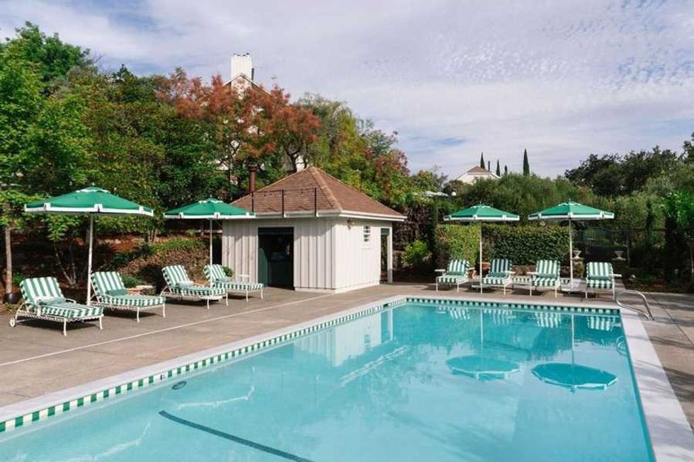 Outdoor pool with striped loungers, green umbrellas, and a small poolside building.