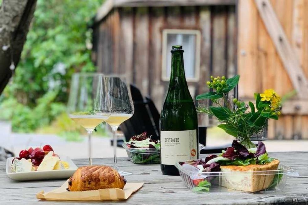 Outdoor table with wine, salad, cheese, fruit, pastry, and flowers.