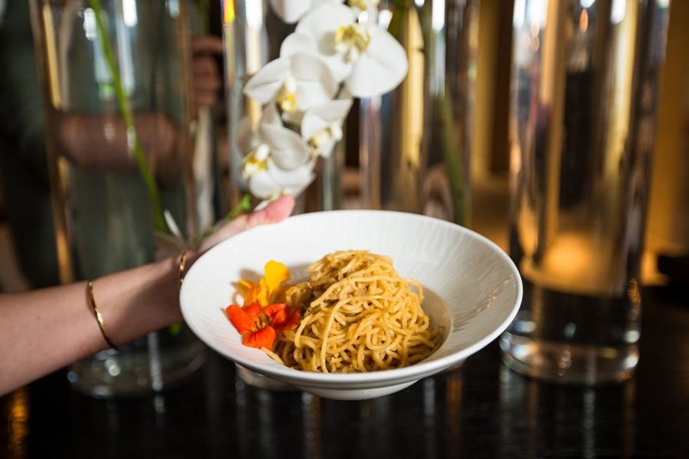 Pasta dish garnished with flowers, held against a background of vases and white orchids.