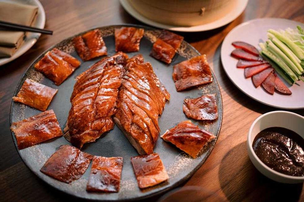 Peking duck platter with crispy skin, garnishes, and sauce on a table.