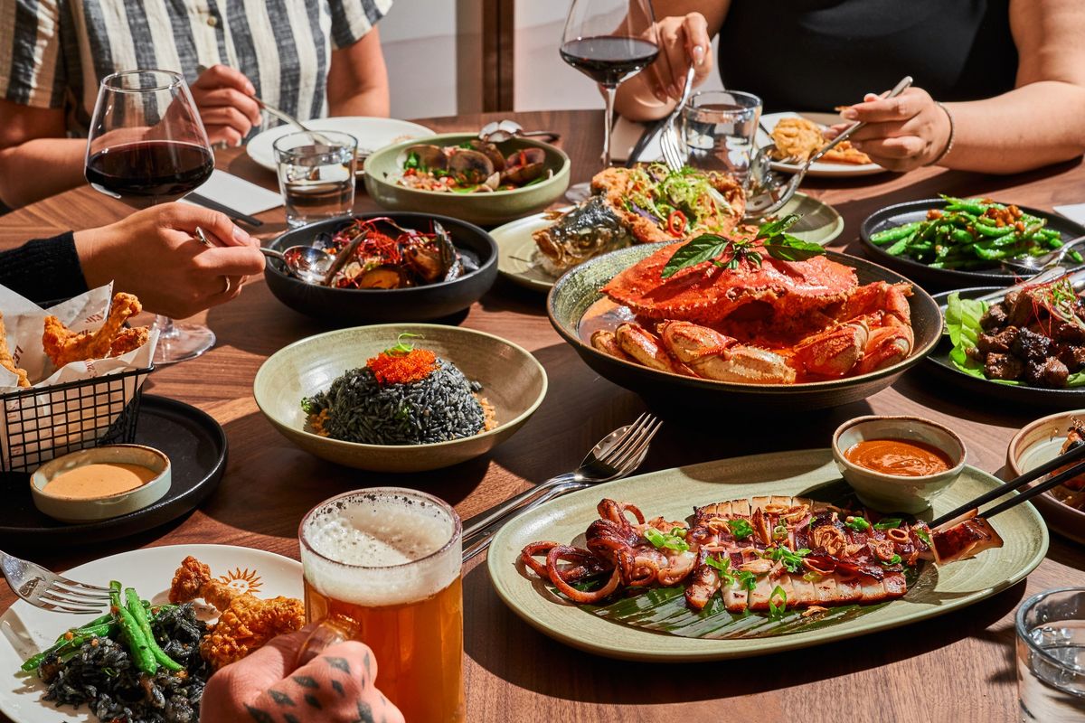 People enjoying a feast with seafood, rice dishes, and drinks on a wooden table.