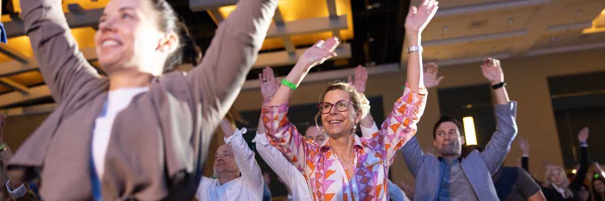 people in a conference audience on their feet with their hands raised and smiling