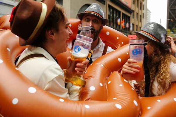 People in Bavarian hats drink beer, surrounded by inflatable pretzels at a festive event.