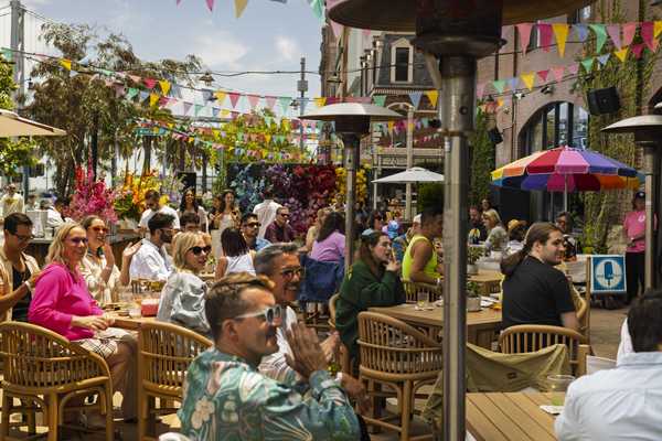 people laughing and clapping at tables outdoors with colorful flags strung overhead