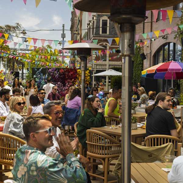 people laughing and clapping at tables outdoors with colorful flags strung overhead
