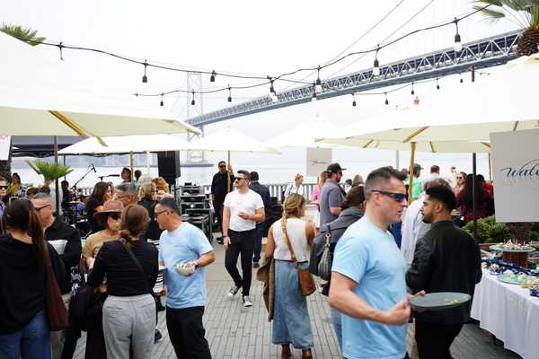 people milling around a patio with umbrellas and tables covered in food