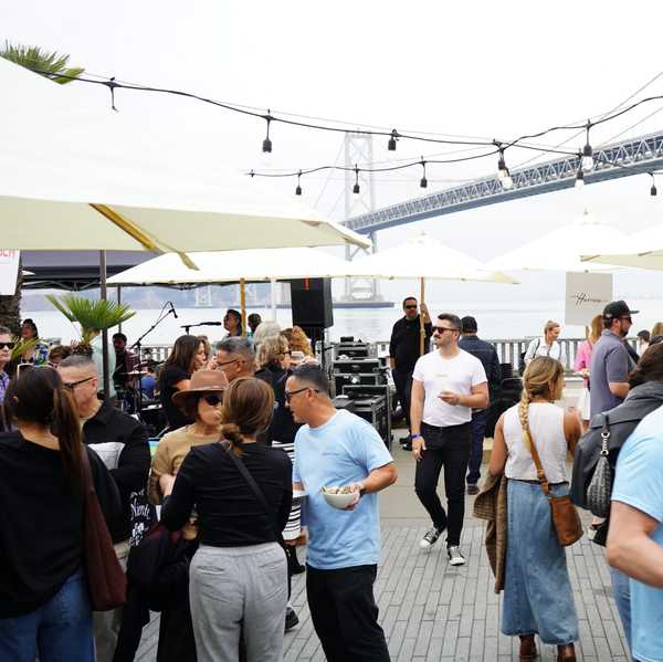 people milling around a patio with umbrellas and tables covered in food