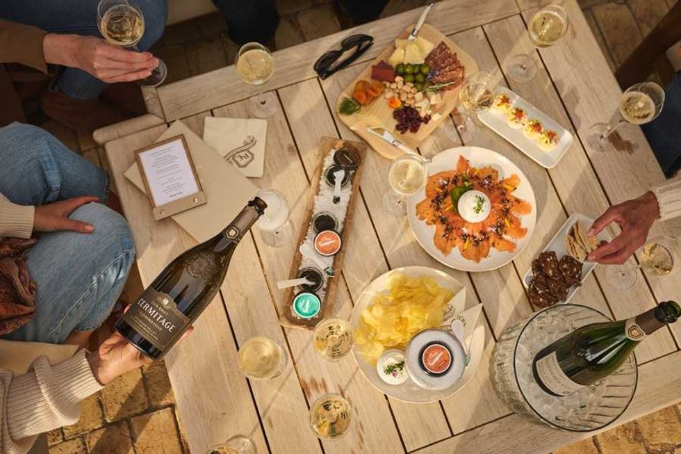 People sharing wine and appetizers on a wooden table outside.